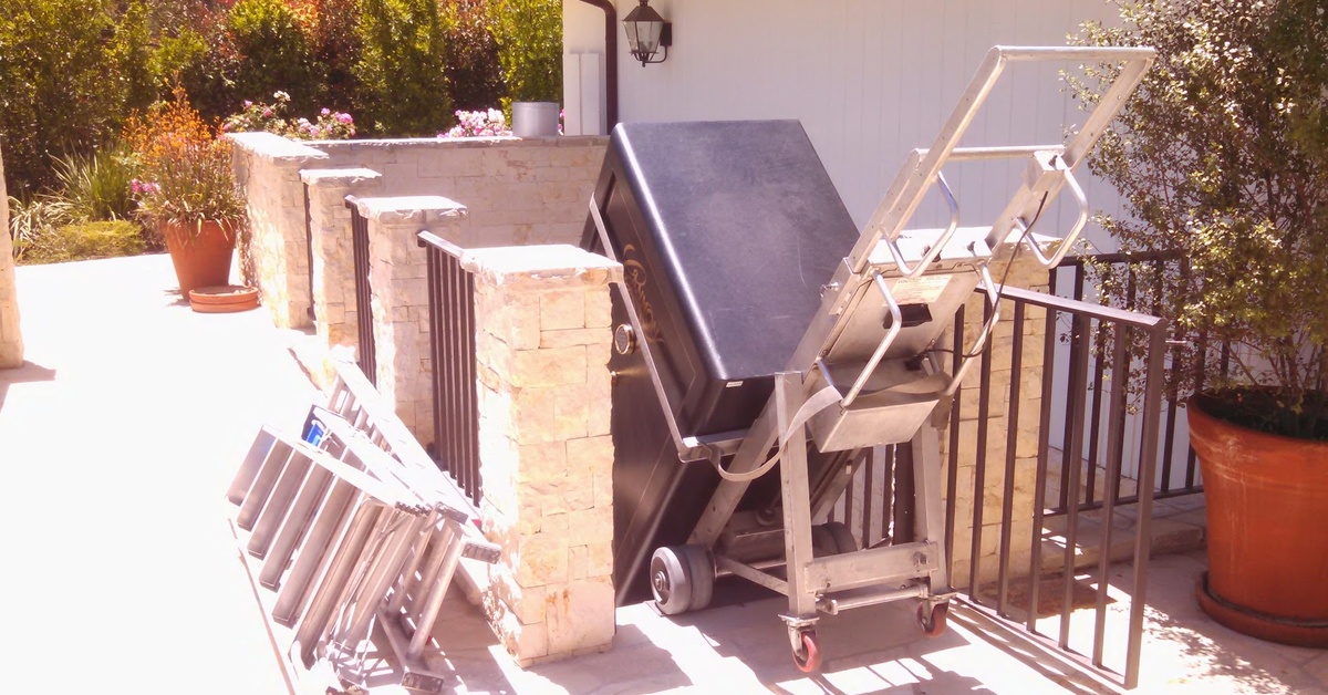  Safe strapped to a powered dolly tilts near a patio stair opening, with metal ramps set on the walkway.